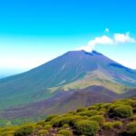 Mount Etna with smoke, greenery, and blue sky.