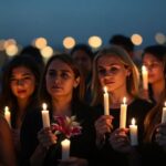 Diverse individuals holding candles in a twilight gathering.