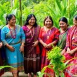Indigenous women in traditional attire sharing stories outdoors.