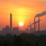 Industrial pollution contrasting with natural greenery at sunset.