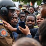 Presidential Guard seizing a journalist's phone during protest.