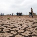 Barren landscape with cracked earth and weary people.