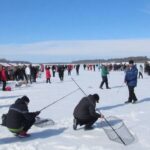 Participants ice fishing on a snowy river landscape.