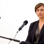 Woman in bright studio with modern microphone, wearing smart suit.