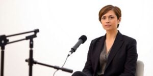 Woman in bright studio with modern microphone, wearing smart suit.