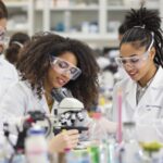 Diverse women and girls in lab coats working together.