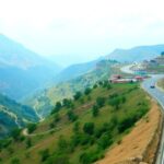 Mountain road in Nepal with lush greenery and vehicles.