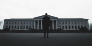 A person stands solemnly, facing a distant, imposing structure.