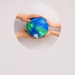 Multiple hands gently cupping a blue and green globe through a circular cutout.