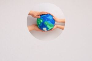 Multiple hands gently cupping a blue and green globe through a circular cutout.