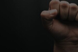 Close-up of a clenched fist against a dark background, showing knuckles and fingers curled in.