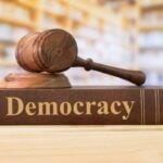 Gavel resting on a book labeled Democracy, symbolizing justice and the rule of law.