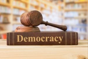 Gavel resting on a book labeled Democracy, symbolizing justice and the rule of law.