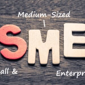 Wooden letters spell 'SME' on a wooden surface, with handwritten notes 'Medium-Sized' above and 'Small & Enterprises' beside—illustrating the SME acronym.