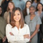 Front-center woman in a white blouse with arms crossed, smiling, standing in front of a diverse group of colleagues.