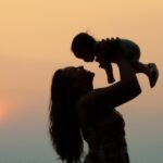 Silhouette of a woman lifting a baby above her head at sunset.