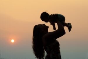 Silhouette of a woman lifting a baby above her head at sunset.