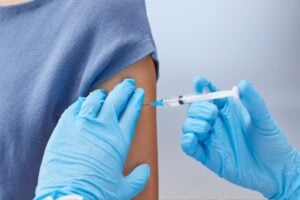 A healthcare professional wearing blue gloves administers a vaccine injection into a patient's upper arm.