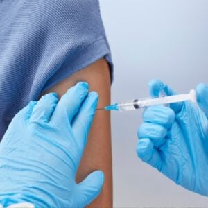 A healthcare professional wearing blue gloves administers a vaccine injection into a patient's upper arm.