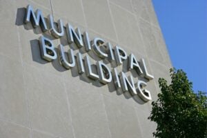 Exterior wall of a municipal building with large metal letters spelling 'MUNICIPAL BUILDING' and a leafy tree nearby.