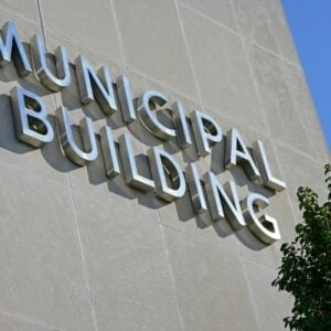 Exterior wall of a municipal building with large metal letters spelling 'MUNICIPAL BUILDING' and a leafy tree nearby.