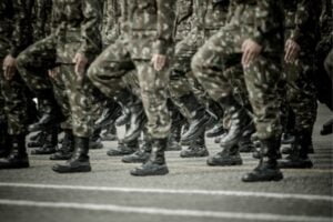 Soldiers in camouflage uniforms marching in formation, showing their boots and lower bodies in step.