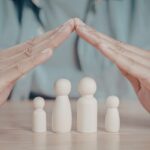Hands hovering over wooden family figures, forming a protective dome shape over them on a table.