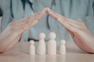 Hands hovering over wooden family figures, forming a protective dome shape over them on a table.