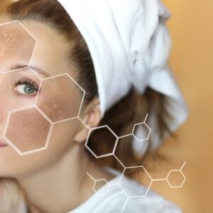 Woman with a towel on her head, touching her face, with a skincare/beauty overlay of hexagonal chemical shapes.