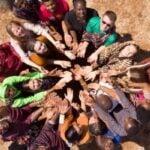 Diverse group forming a circle from above, hands joined in the center to symbolize teamwork and unity.