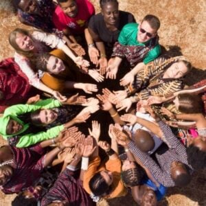 Diverse group forming a circle from above, hands joined in the center to symbolize teamwork and unity.