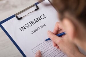 Close-up of a hand writing on an insurance claim form clipped to a blue clipboard.