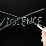 Hand erasing the word 'VIOLENCE' crossed out on a chalkboard, signaling anti-violence.