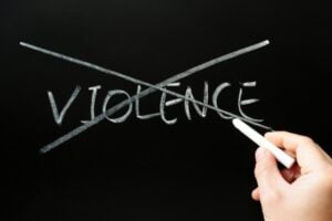 Hand erasing the word 'VIOLENCE' crossed out on a chalkboard, signaling anti-violence.