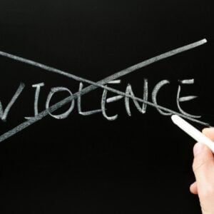 Hand erasing the word 'VIOLENCE' crossed out on a chalkboard, signaling anti-violence.