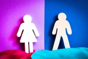 White paper cutouts of a girl and a boy stand on opposite colored backgrounds (pink left, blue right) with a vertical color split between them, suggesting gender division.