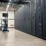 Data center aisle with rows of server racks on both sides and a wheeled cart with a monitor at the far end.