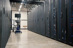 Data center aisle with rows of server racks on both sides and a wheeled cart with a monitor at the far end.