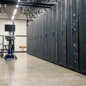 Data center aisle with rows of server racks on both sides and a wheeled cart with a monitor at the far end.