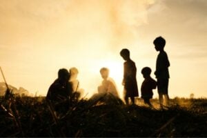 Silhouetted children playing in a field at sunset with a warm golden sky