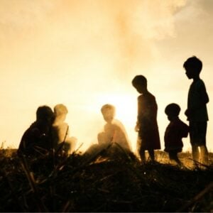 Silhouetted children playing in a field at sunset with a warm golden sky