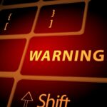 Close-up of a keyboard with a glowing red 'WARNING' indicator and code-like symbols, suggesting a warning or error message.