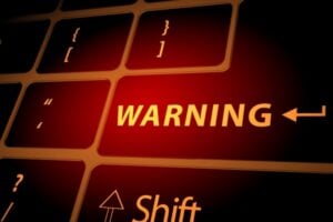 Close-up of a keyboard with a glowing red 'WARNING' indicator and code-like symbols, suggesting a warning or error message.
