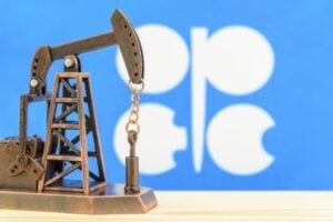 Miniature oil pump jack model on a wooden surface with a blue backdrop and white shapes in the background.