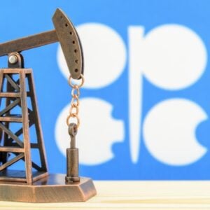 Miniature oil pump jack model on a wooden surface with a blue backdrop and white shapes in the background.