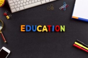 Colorful letters spelling EDUCATION on a dark desk surrounded by school supplies like a keyboard, notebook, clips, and markers.