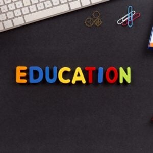 Colorful letters spelling EDUCATION on a dark desk surrounded by school supplies like a keyboard, notebook, clips, and markers.