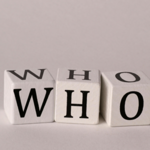 Three white letter blocks arranged on a pale surface spell 'WHO' (W, H, O).