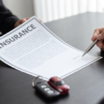Two people sign an insurance contract at a desk, with car keys placed nearby on the table.