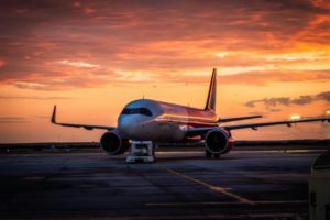 Commercial airliner parked on the tarmac at sunset, warm orange sky.